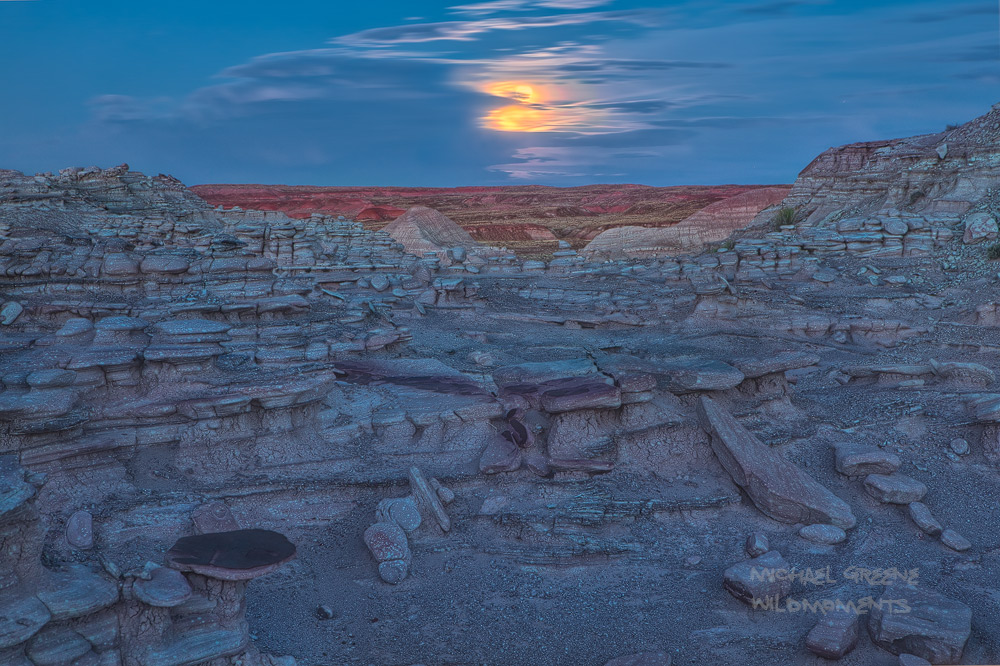 The full moon appears from behind a thick veil of clouds above the painted desert in the black forest area of Petrified Forest...