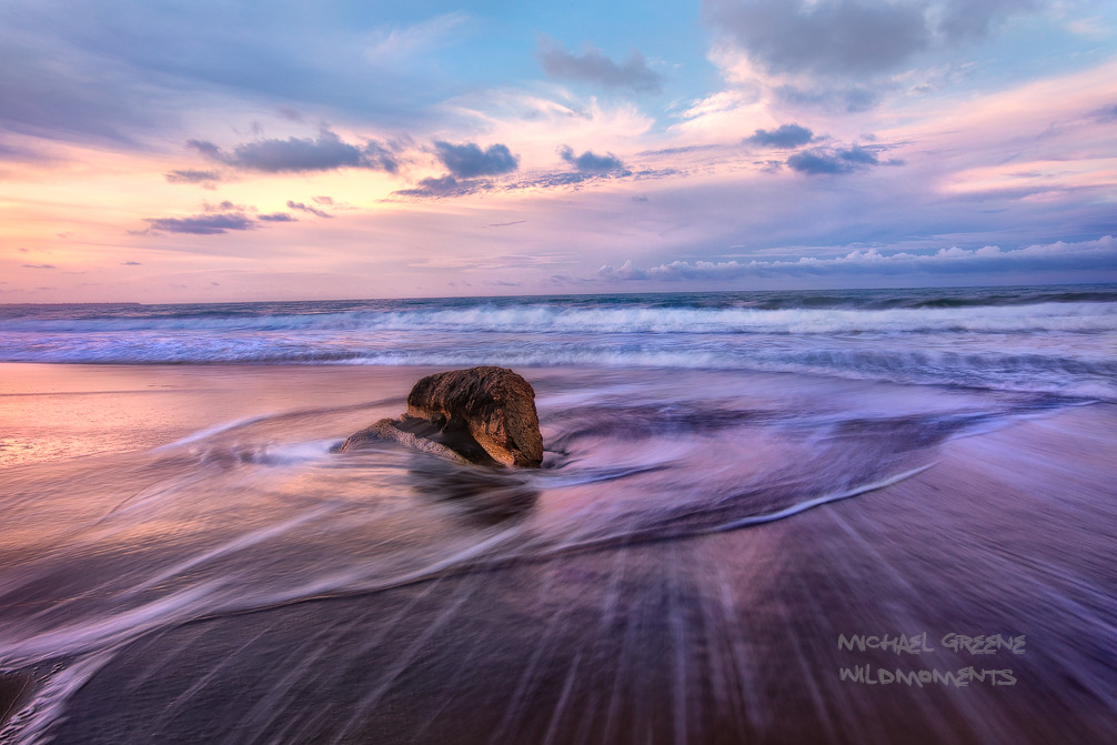 A sandstone curiosity is circled by swirling surf at sunset on a beautiful summer evening at the Playa Negra. This beach is located...