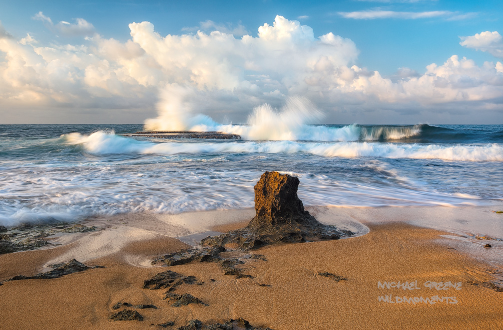 A lone sandstone formation decorates the beach near a rocky platform amid exploding Caribbean surf and dramatic clouds. This...