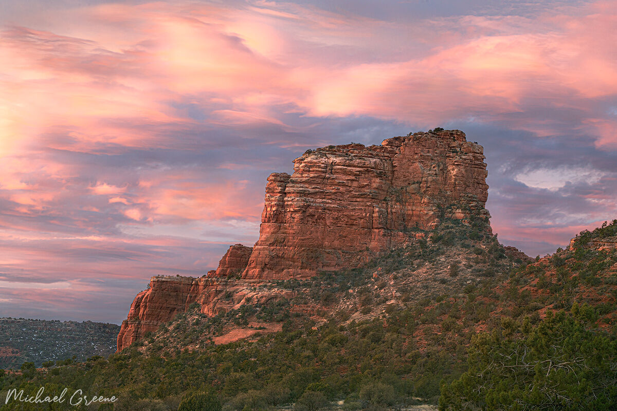 A stormy sunrise of a distant butte brings vibrant colors to the sky near the Village of Oak Creek, AZ.