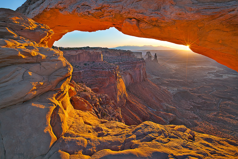 The sun beckons over the La Sal Mountains (12,721 ft)&nbsp;as seen through Mesa Arch in Canyonlands National Park.